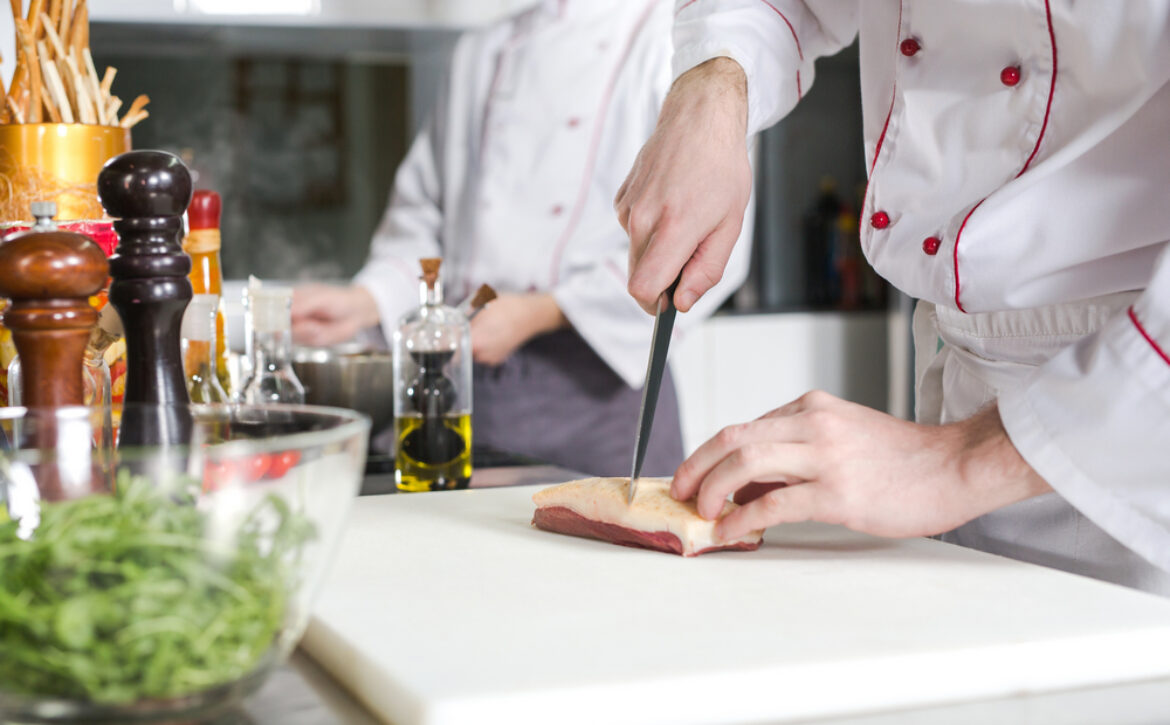 Chef cutting meat on chopping board, professional cook holding k